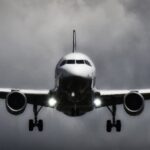 A dramatic view of an airplane landing with stormy clouds overhead, showcasing aviation in a monochrome scene.