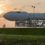 A space shuttle on a launchpad with people walking nearby at sunset.