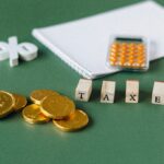 Close-up of tax-related items including coins, calculator, and word 'taxes' on a green background.