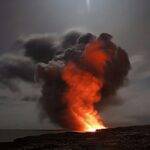 Volcanic eruption with smoke and lava under a starry night sky.